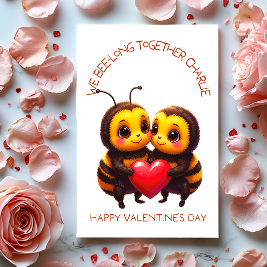 Valentine's Day card with two bees holding a heart and the text 'We bee-long together' and Happy valentines Day' surrounded by flowers and petals.