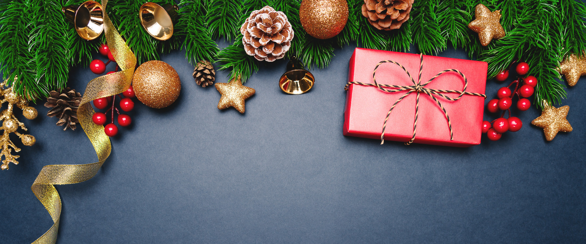 Decorative Christmas scene with a red gift box, greenery, ornaments, and ribbons on a dark blue background.