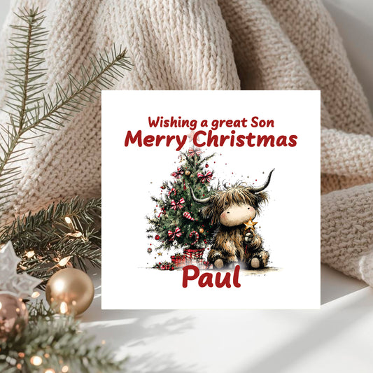 Christmas card with a cartoon Highland cow and Christmas tree, placed on a knitted surface with festive decorations.