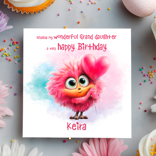 Birthday card with a colorful  monster character holding a heart, surrounded by flowers and sprinkles on a gray background.
