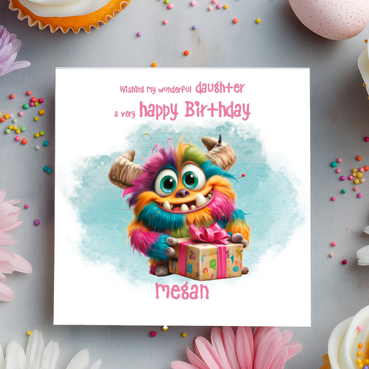 Birthday card with a colorful monster holding a gift, surrounded by flowers and sprinkles on a light gray background.