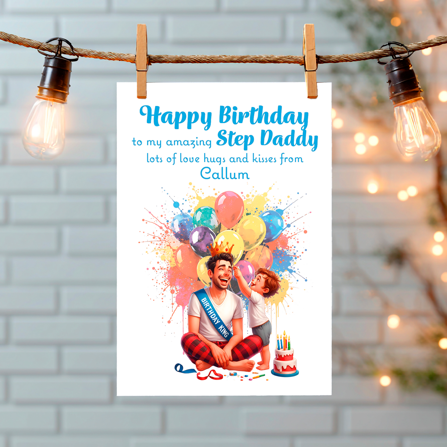 A Birthday card with an illustration of a young Boy placing a crow and his Dads head with a birthday cake and balloons behind them and a personalised message that can be personalised for Dad,Daddy,Step Daddy or Step Dad. hanging from a string with lights on a white  wall background.