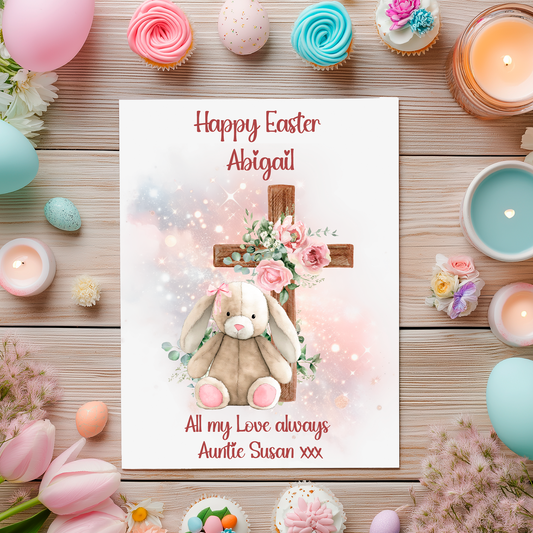 Easter-themed card with a  pink bunny and cross design, surrounded by Easter decorations on a wooden surface. Can be personalised with name and relation